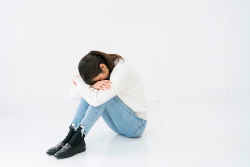 膝を抱えて悩んでいるママの写真